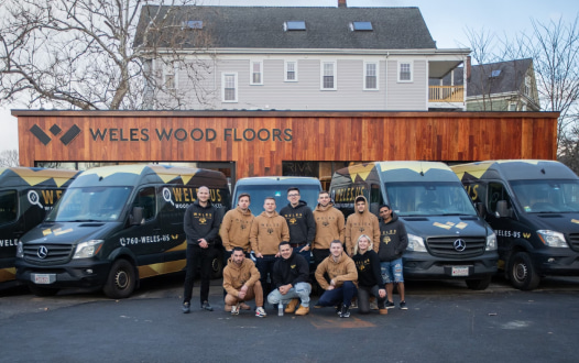 Weles team smiling in front of their service vans and showroom.