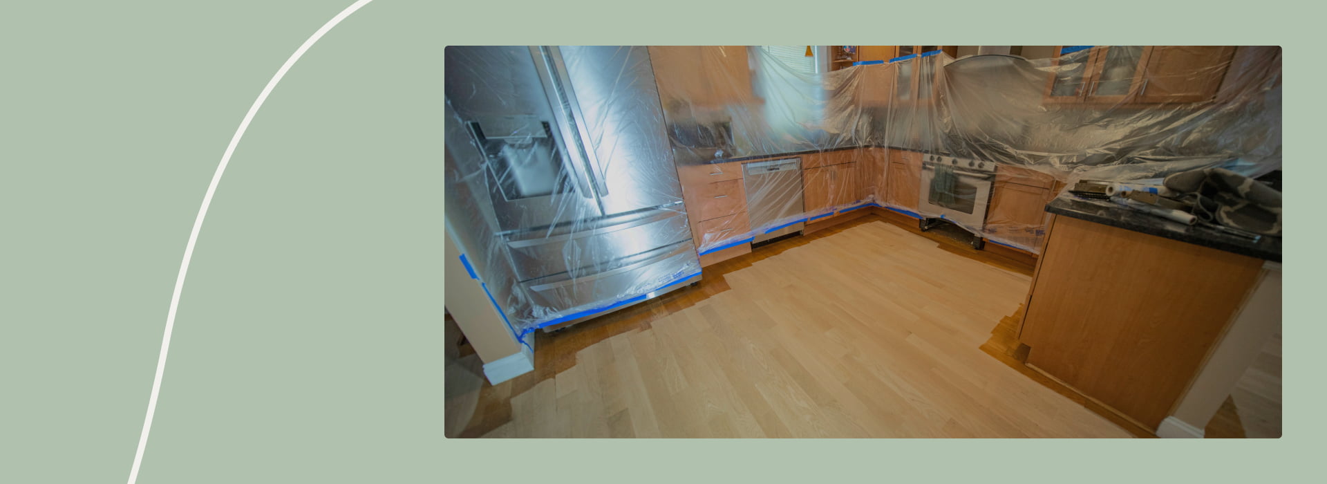 Kitchen area prepared for refinishing hardwood floors, with appliances and counters covered in plastic sheeting for protection