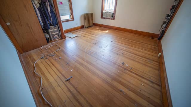 Empty bedroom with a worn hardwood floor, the finish dulled and scratched across the boards, ready for a full refinish.