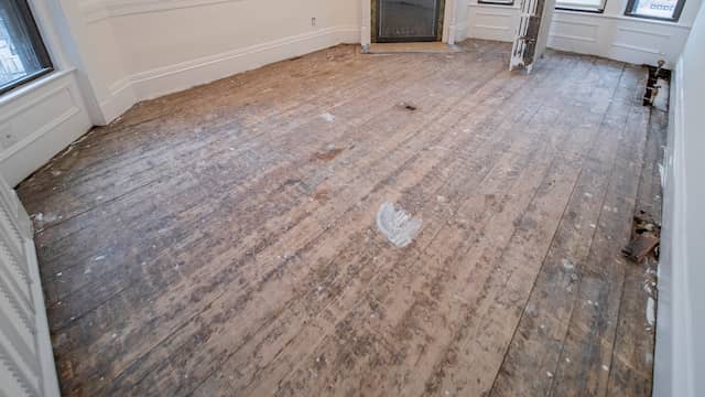 Badly damaged floor with gouged gray boards, wide gaps, and paint spatter, worn past the point where sanding helps.
