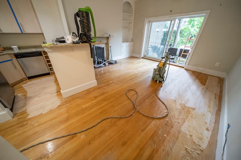 Living room under renovation showing partially stained hardwood flooring, illustrating the transformative process of floor finishing by Weles.