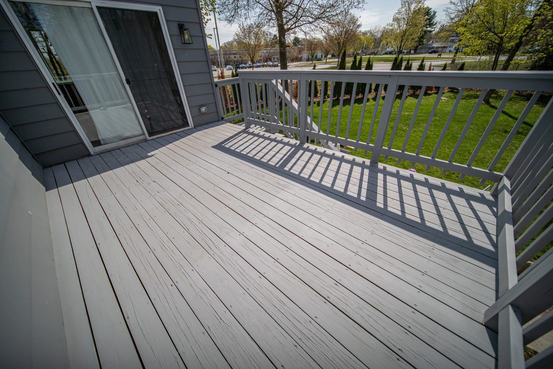 Weathered, water-damaged deck boards sanded and refinished in light gray by Weles, railing shadows across the new finish.
