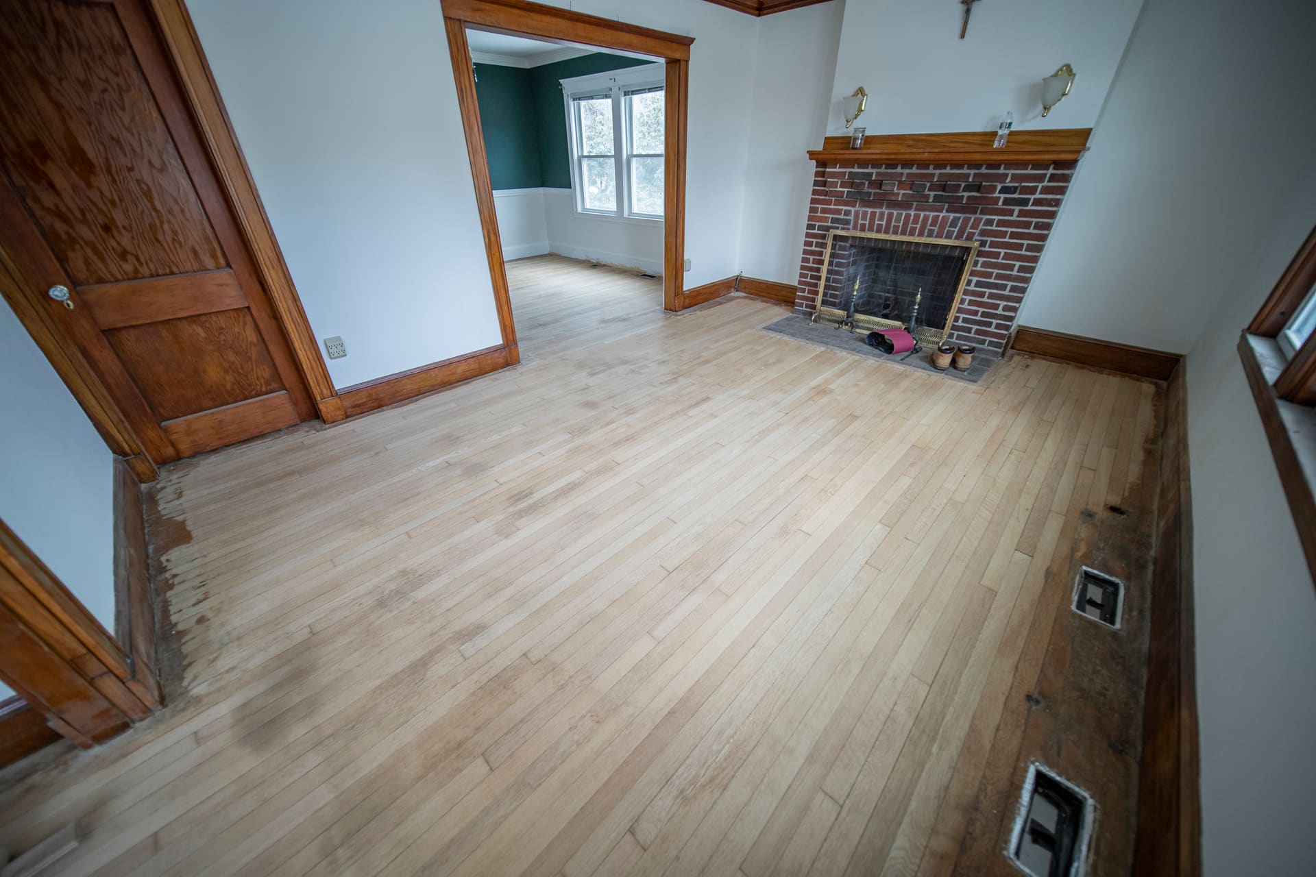 Freshly sanded oak floor with dark water staining running along the wall under the windows, before board replacement.